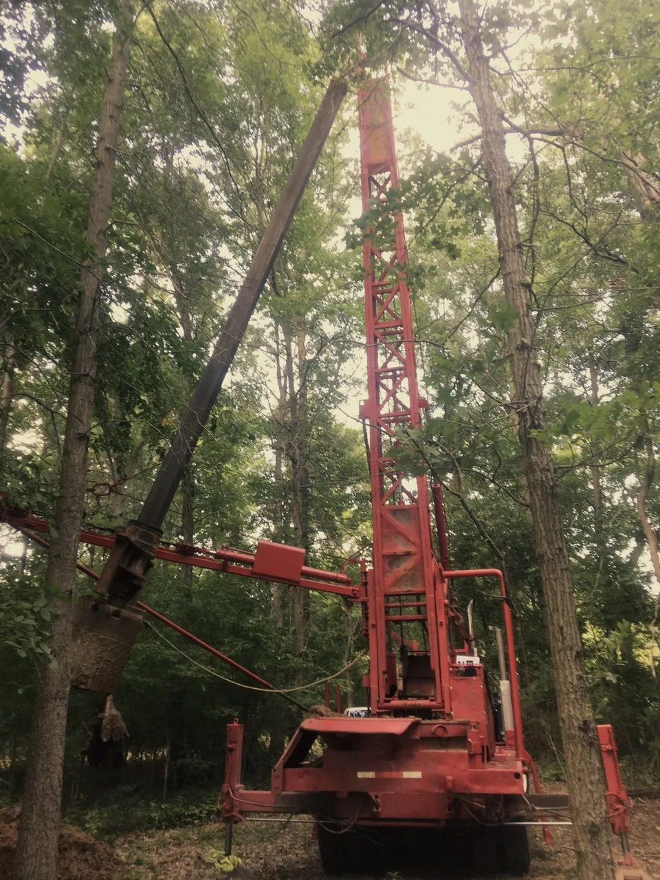 Lincoln Pump's drill rig with the mast raised, drilling a new water well in wooded ground in eastern Missouri