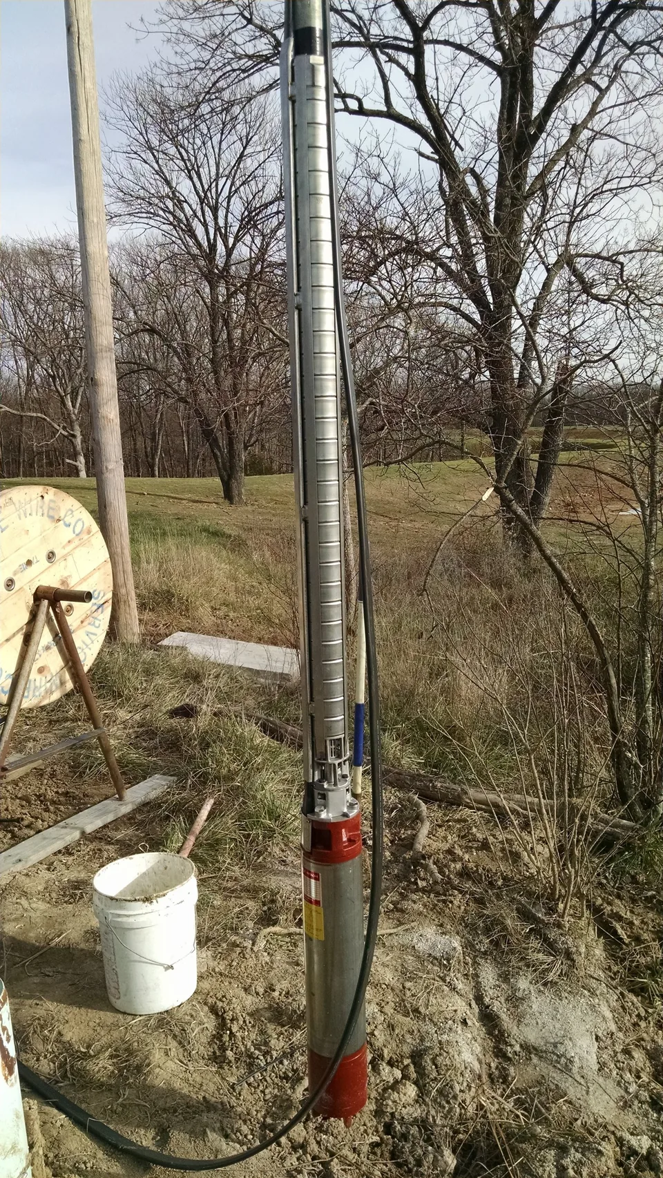 A stainless submersible pump and motor on the drop pipe at the wellhead, ready to be set down the casing